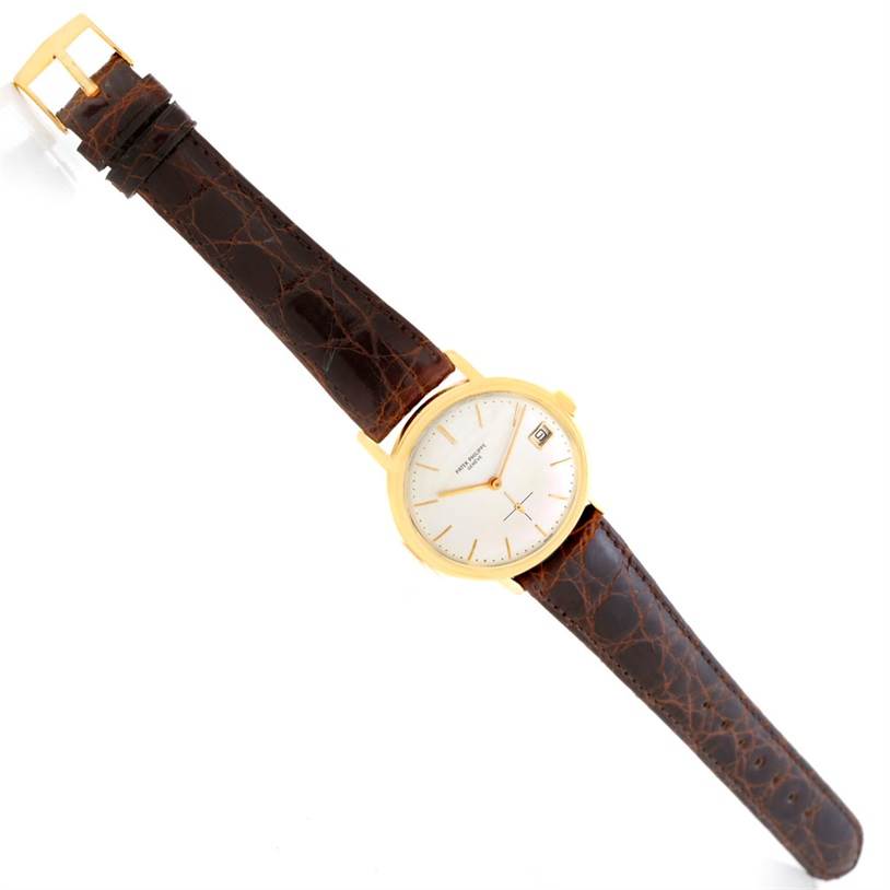 The image shows a Vintage Patek Philippe watch with a leather strap, gold case, and a white dial, viewed from a top-down angle.