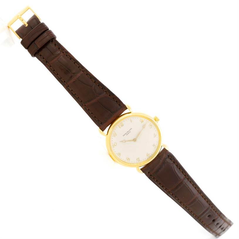 This image shows a vintage Patek Philippe watch with a gold case, brown leather strap, and a white dial, viewed from a top-down angle.