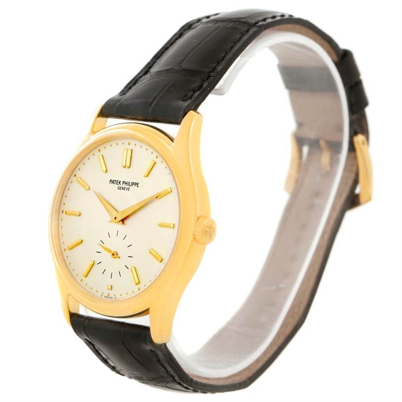 The image shows a side and angled view of a Patek Philippe Calatrava 5023 Men's Yellow Gold Silver Dial 5023 Men's Yellow Gold Silver Dial watch with a gold case, cream dial, and black leather strap.
