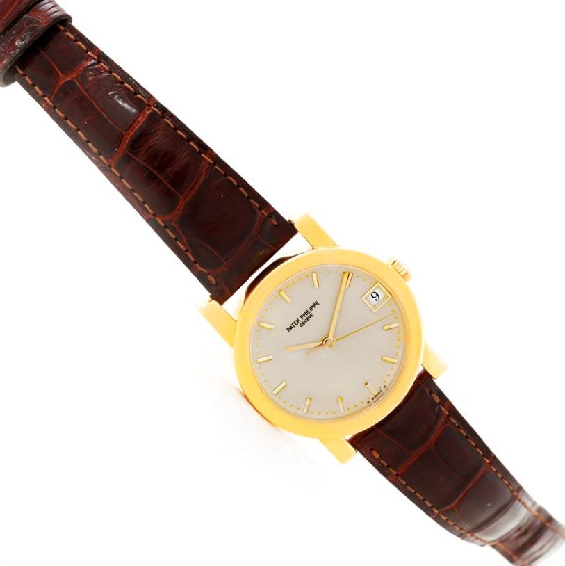 The image shows a Patek Philippe Calatrava 5012 Men
s Yellow Gold Beige Dial 5012 Men
s Yellow Gold Beige Dial watch at a slight angle, featuring its dial, leather strap, and gold casing.