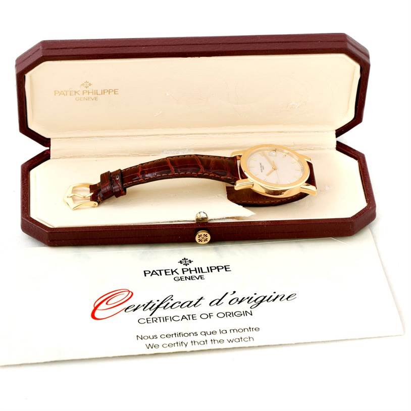 The image shows a Patek Philippe Calatrava 5012 Men
s Yellow Gold Beige Dial 5012 Men
s Yellow Gold Beige Dial watch angled slightly to display the face and strap, inside its case with a certificate of origin.