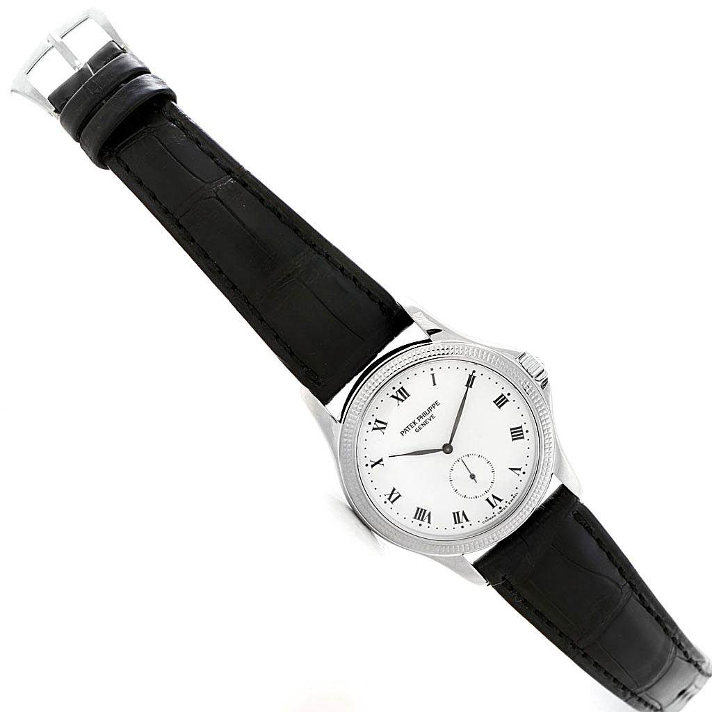 The image shows a Patek Philippe Calatrava 5115G Men
s White Gold White Dial 5115G Men
s White Gold White Dial watch at an oblique angle, displaying its face, bezel, and black leather strap.