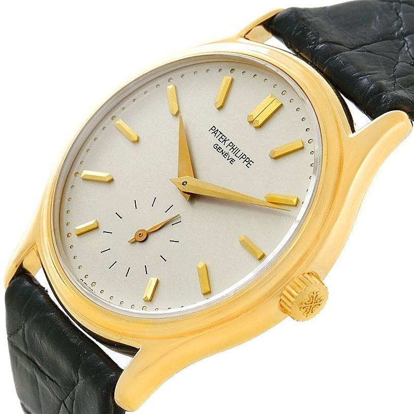 The Calatrava model by Patek Philippe is shown from a slightly tilted front angle, highlighting its dial, yellow gold case, and black leather strap.