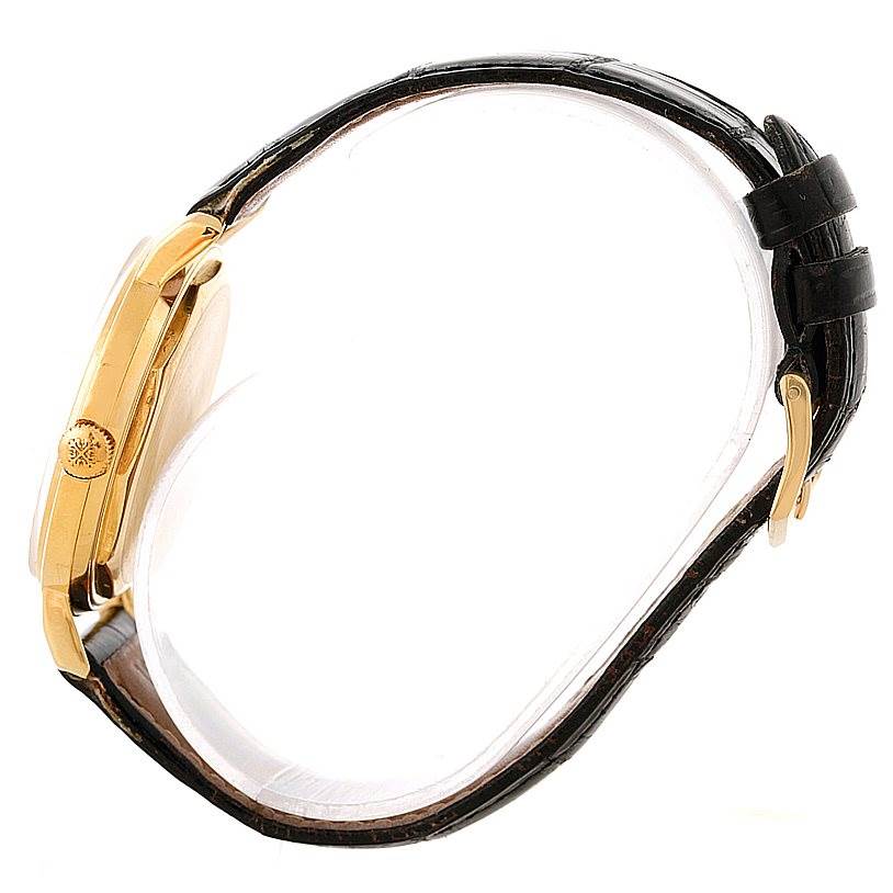 This side view image shows the case, crown, and black leather strap of a vintage Patek Philippe watch.