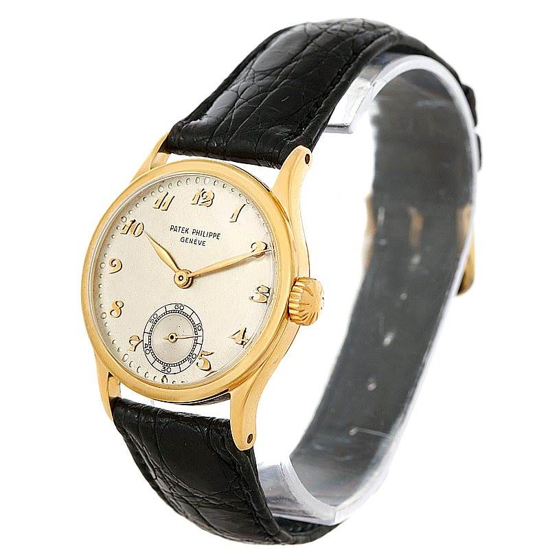 The Patek Philippe Vintage watch is shown at an angle, highlighting its gold case, dial, crown, and black leather strap.