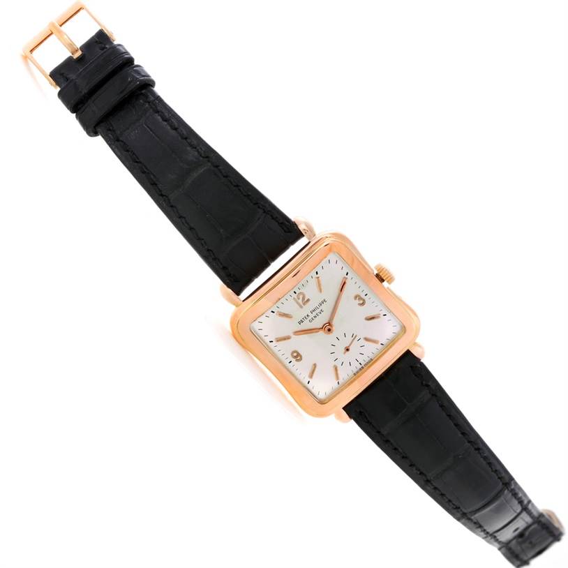 The image shows a Patek Philippe Calatrava 2493 Men's Rose Gold Silver Dial 2493 Men's Rose Gold Silver Dial watch with a rectangular face, black strap, and gold casing at a slightly angled top view.