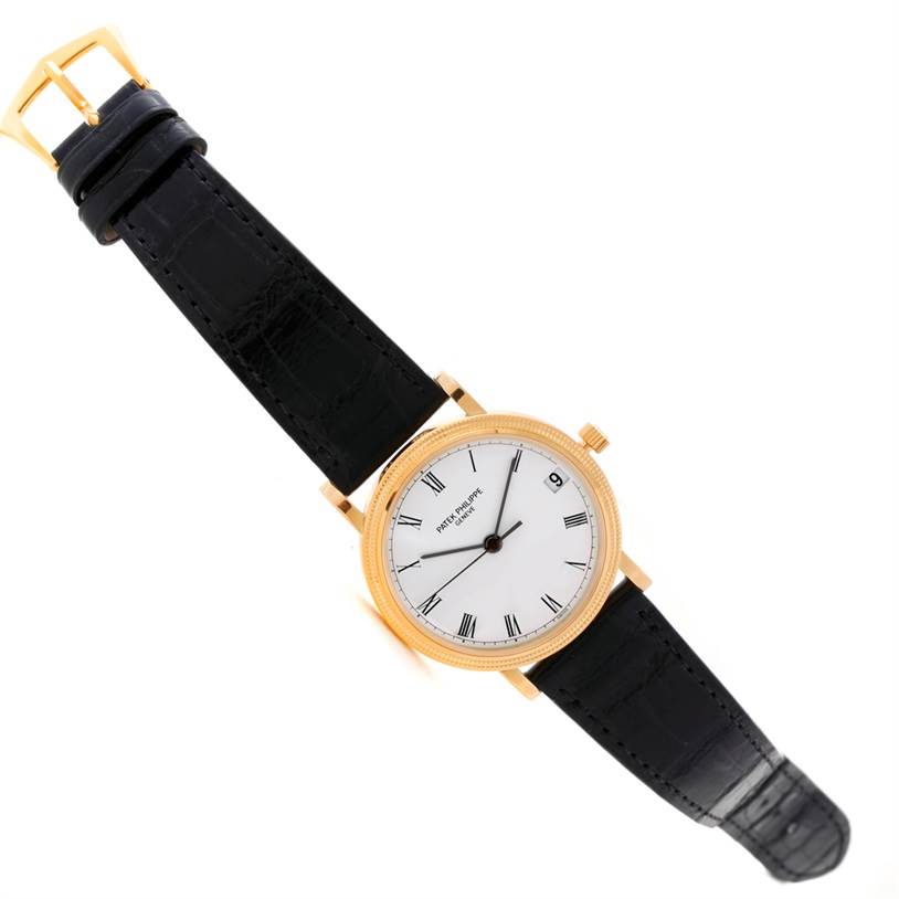 The image shows a top view of a Patek Philippe Calatrava 3802 Men's Yellow Gold White Dial 3802 Men's Yellow Gold White Dial watch, highlighting its black leather strap and gold case.
