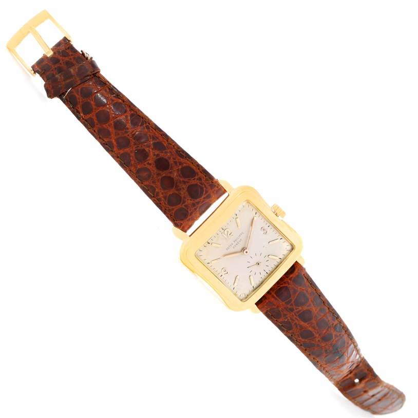 This image shows a top-down view of a vintage Patek Philippe watch with a brown leather strap and a square gold case.