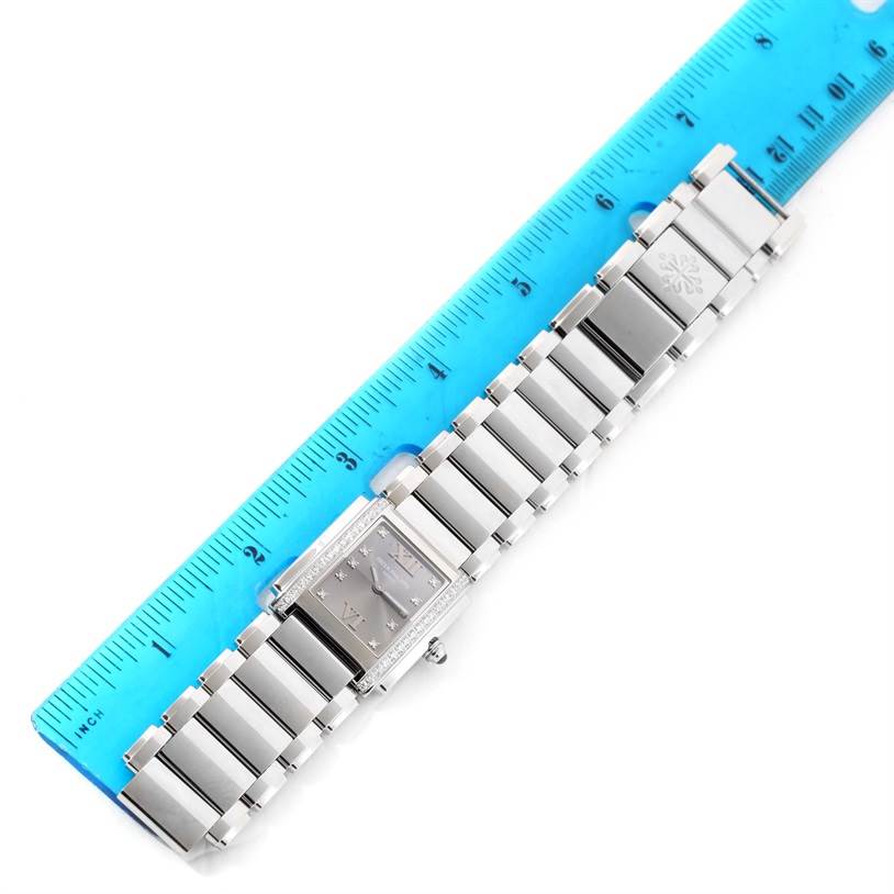 The image shows a Patek Philippe Twenty-4 4910/10A-010 Women's Stainless Steel Grey Dial 4910/10A-010 Women's Stainless Steel Grey Dial watch laid alongside a blue ruler, displaying the watch's face and metallic band.