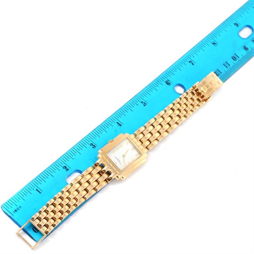 The Patek Philippe Gondolo 4824 Women's Yellow Gold White Dial 4824 Women's Yellow Gold White Dial watch shown is laid flat beside a ruler, displaying its gold bracelet and square face from a top-down perspective.