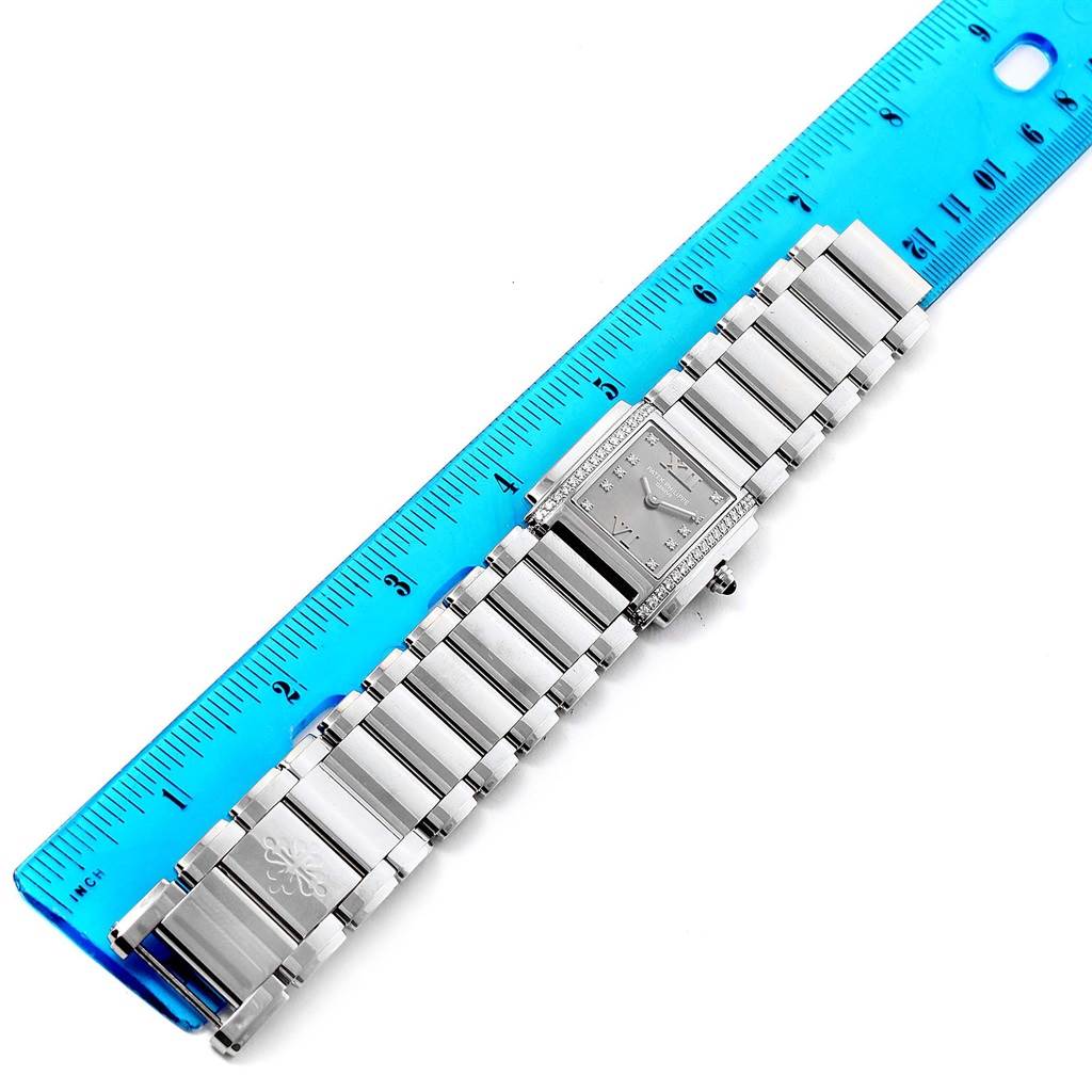 The image shows a top-down view of a Patek Philippe Twenty-4 4910/10A-010 Women's Stainless Steel Grey Dial 4910/10A-010 Women's Stainless Steel Grey Dial watch next to a blue ruler for scale.