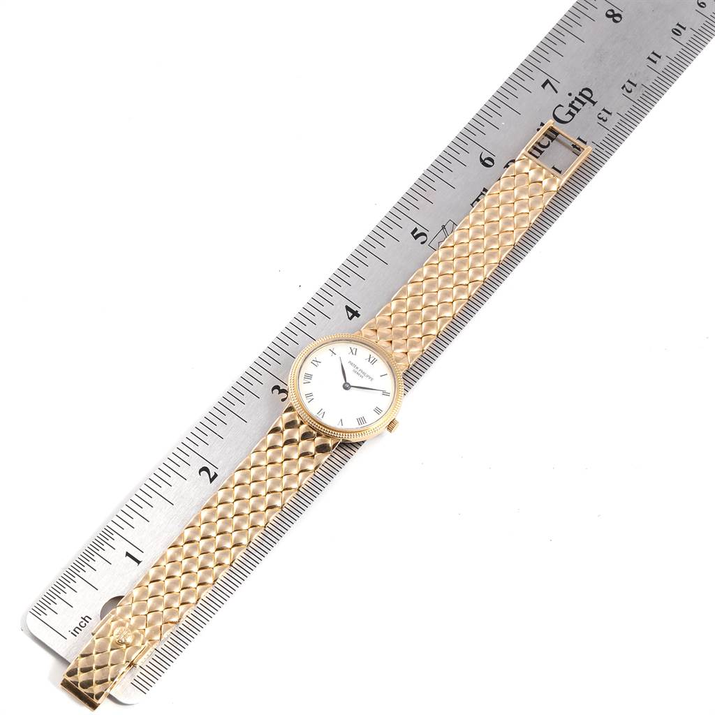 The Patek Philippe Calatrava 4819 Women's Yellow Gold White Dial 4819 Women's Yellow Gold White Dial watch is shown flat, with its gold strap and face aligned next to a ruler.