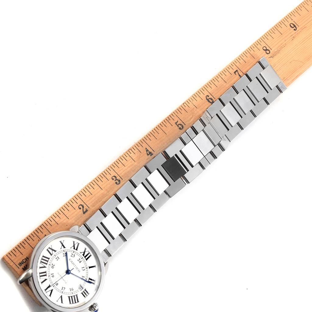 The image shows a top-down view of a Cartier Ronde W6701011 Men
s Stainless Steel Silver Dial W6701011 Men
s Stainless Steel Silver Dial watch and its metal band alongside a wooden ruler for measurement.