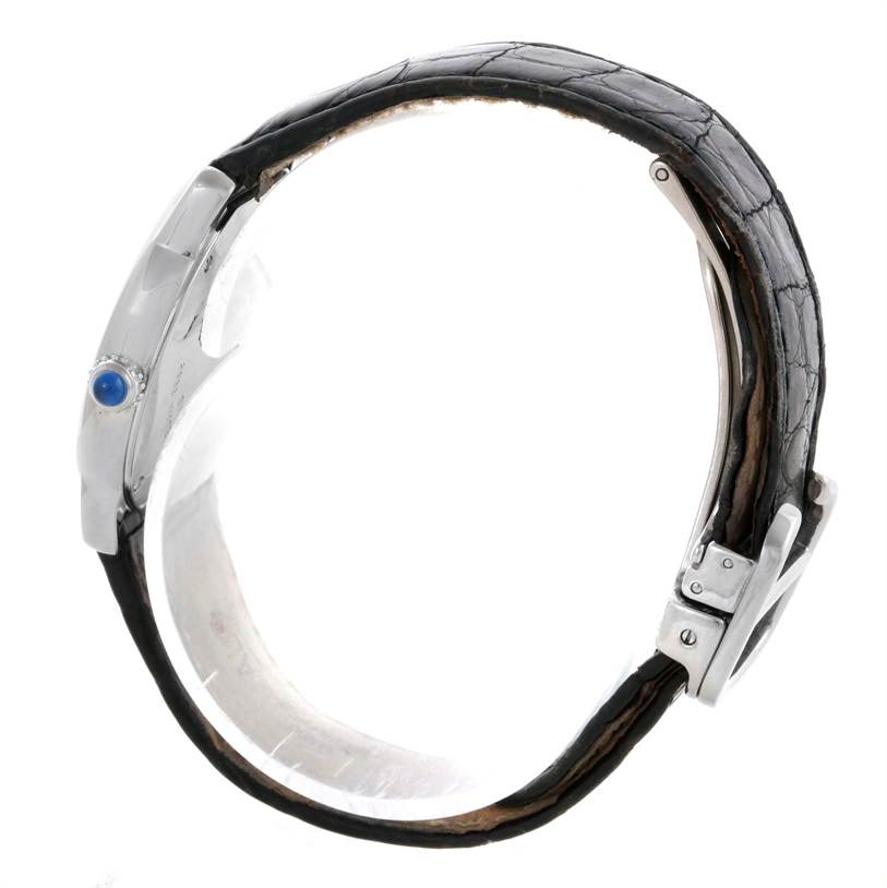 The image shows a side view of a Cartier Ronde W6700155 Women
s Stainless Steel Silver Dial W6700155 Women
s Stainless Steel Silver Dial watch highlighting the crown with a blue cabochon and part of the leather strap.