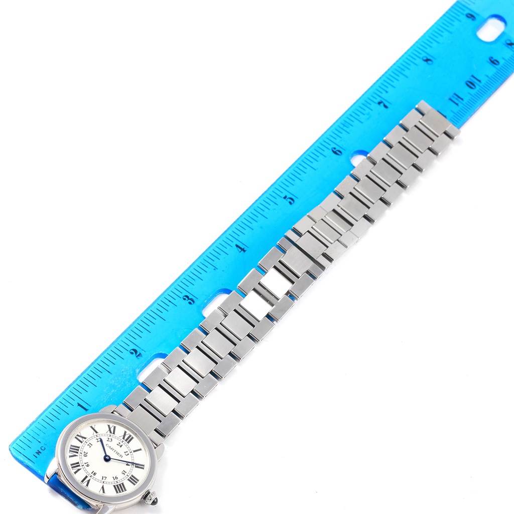The Cartier Ronde W6701004 Women
s Stainless Steel Silver Dial W6701004 Women
s Stainless Steel Silver Dial model is shown from a top-down angle, displaying the watch face and metal strap next to a blue ruler.