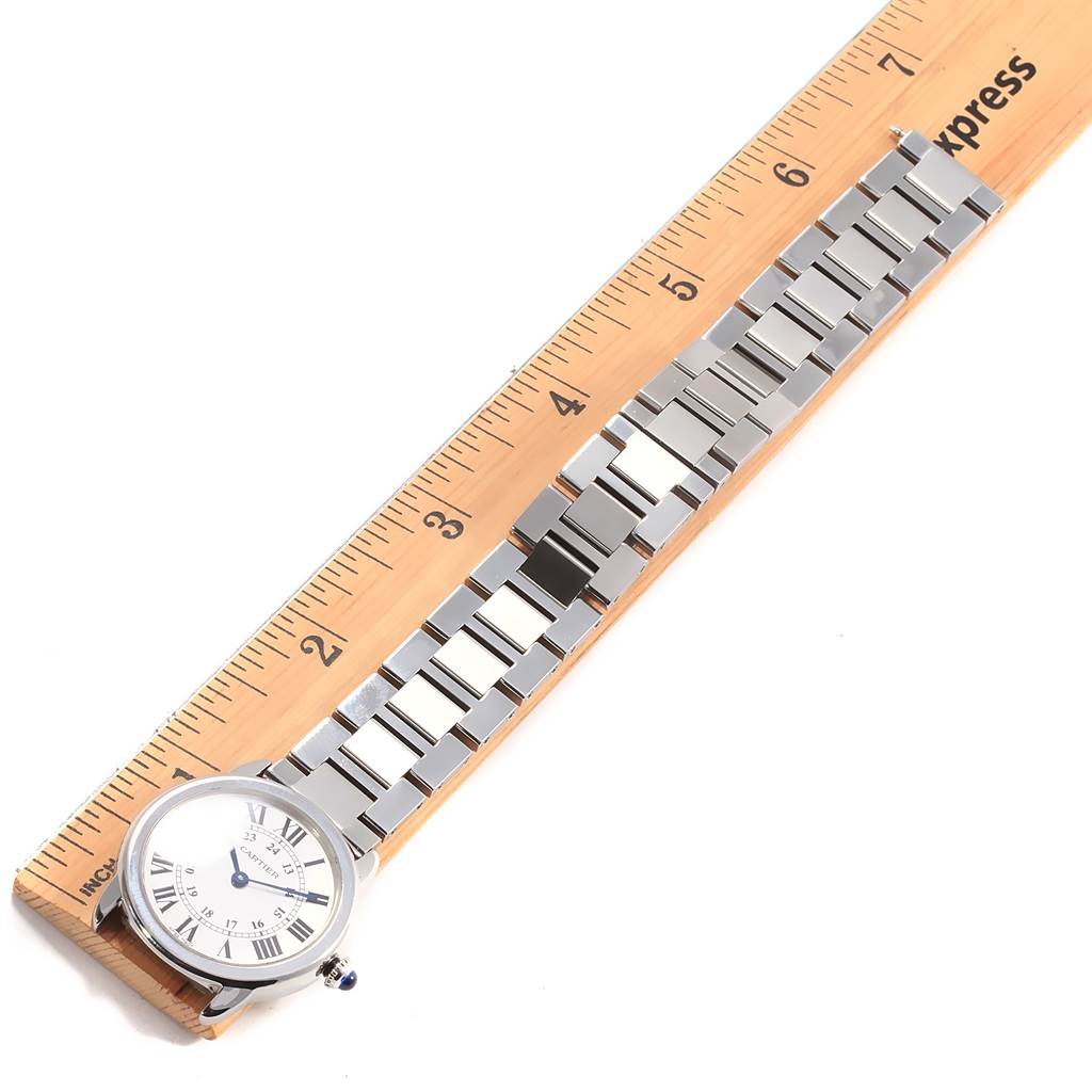 The Cartier Ronde W6701004 Women's Stainless Steel Silver Dial W6701004 Women's Stainless Steel Silver Dial watch is shown laid flat with a focus on its face, bracelet, and partial clasp, alongside a ruler for scale.