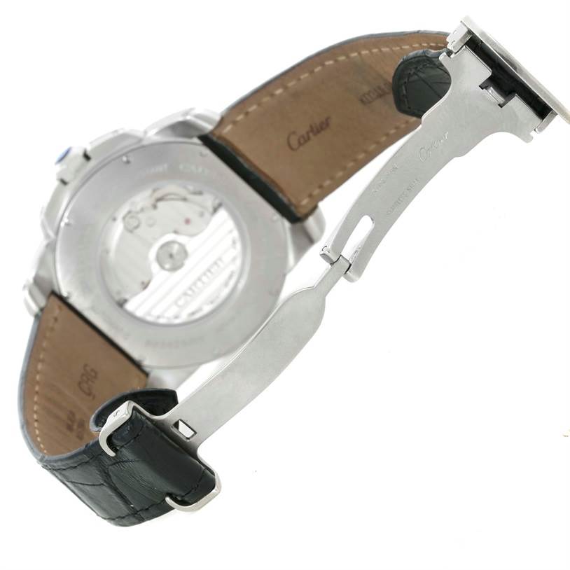 The image shows the back of the Calibre de Cartier watch by Cartier, highlighting the movement and partially opened clasp and leather strap.