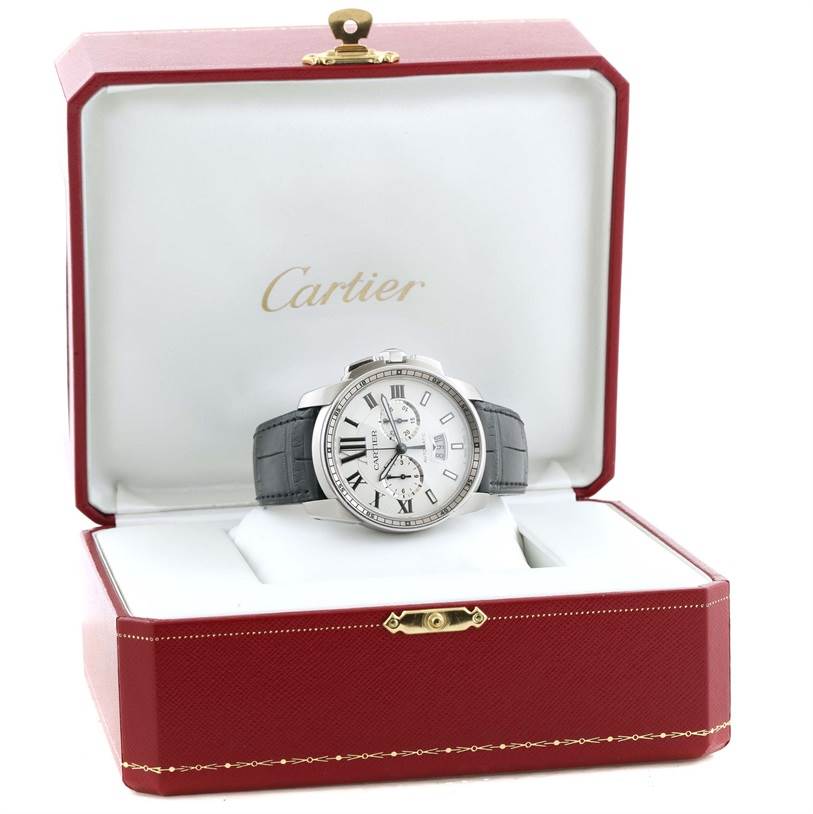 The image shows a front view of a Calibre de Cartier watch by Cartier inside an open red and white Cartier box.