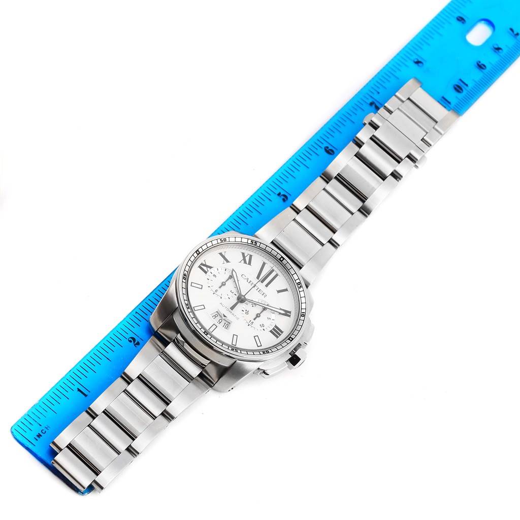 The image shows a top-down view of a Calibre de Cartier watch by Cartier, including the face and bracelet next to a ruler.