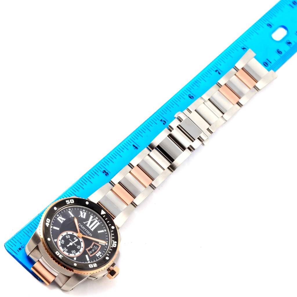 The image shows the Calibre de Cartier watch laid flat, next to a blue ruler, highlighting its band length and face details.