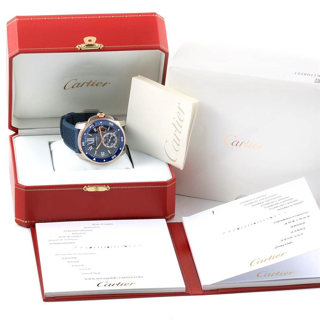 The image shows a Calibre de Cartier watch in its open red case with accompanying documents and accessories neatly placed around.