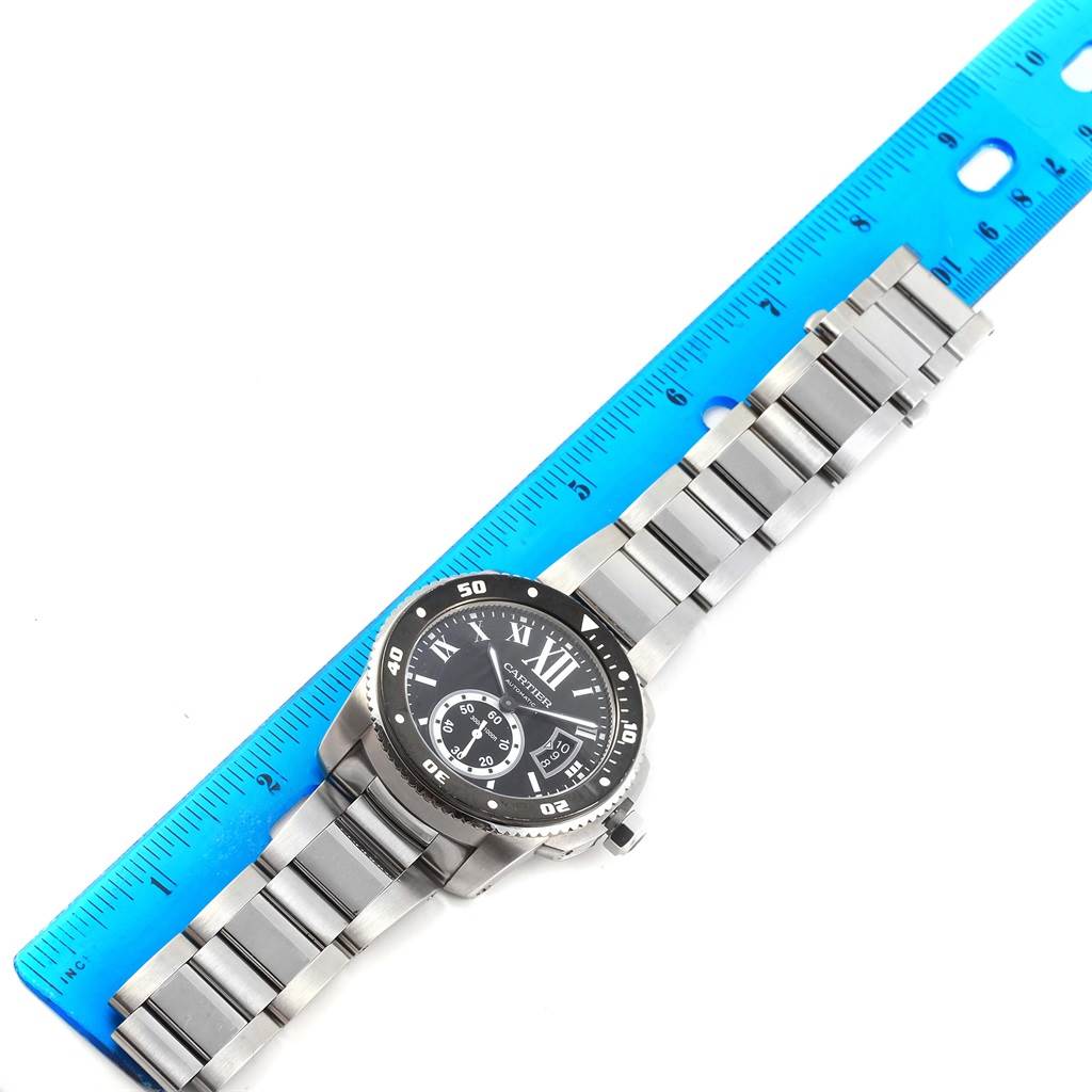 The image shows a Calibre de Cartier watch by Cartier, laid flat with a blue ruler measuring its length.