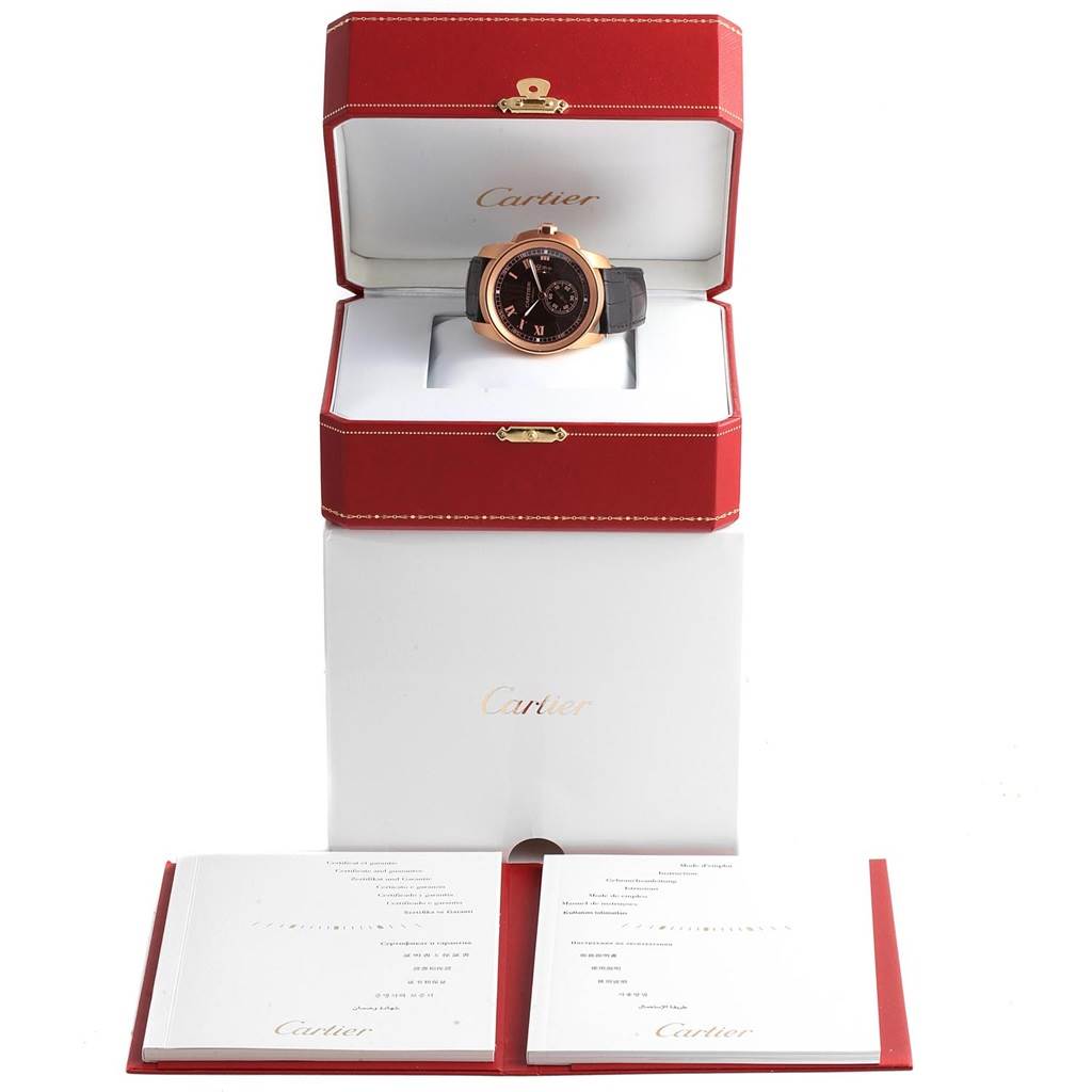 The image shows a front view of a Calibre de Cartier watch by Cartier in an open box with accompanying documents below.