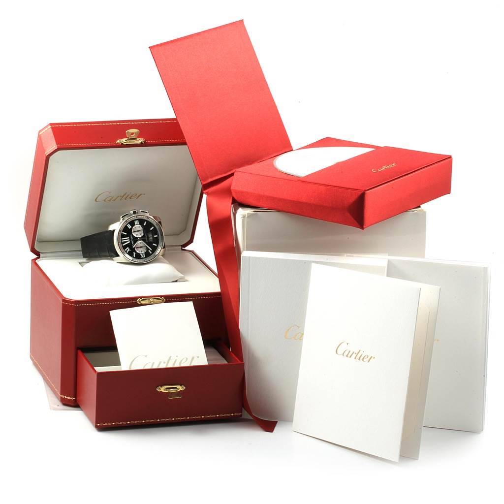 The image shows a Calibre de Cartier watch in its open red box, with additional Cartier packaging and booklets nearby.
