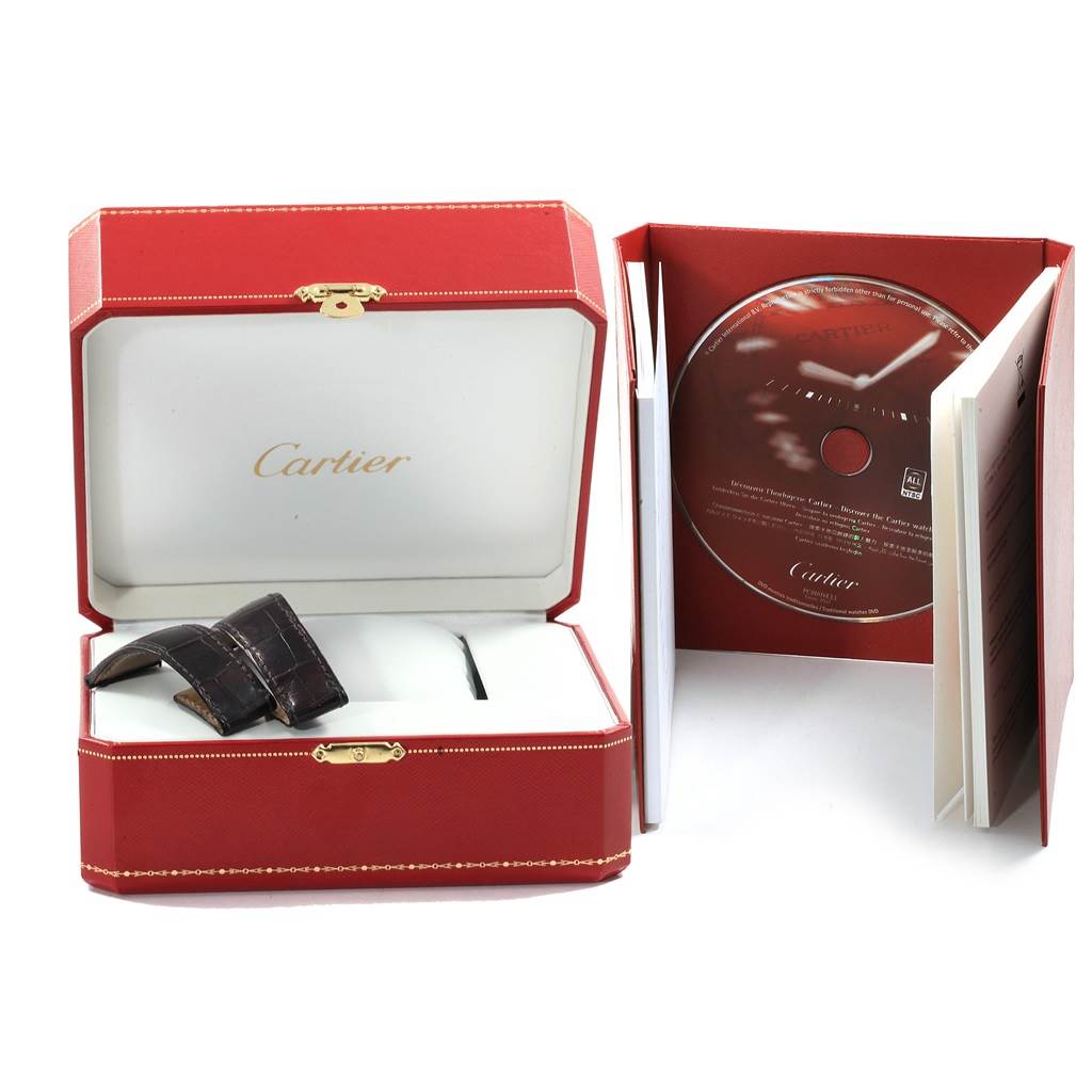 The image shows the Cartier Calibre de Cartier W7100037 Men's Stainless Steel Silver Dial W7100037 Men's Stainless Steel Silver Dial watch's red box, a leather strap, a booklet, and a CD, all from a side angle.