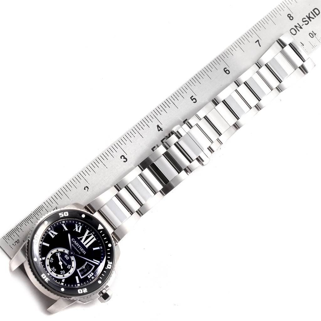 The image shows a Calibre de Cartier watch by Cartier, with a ruler measuring its stainless steel bracelet.