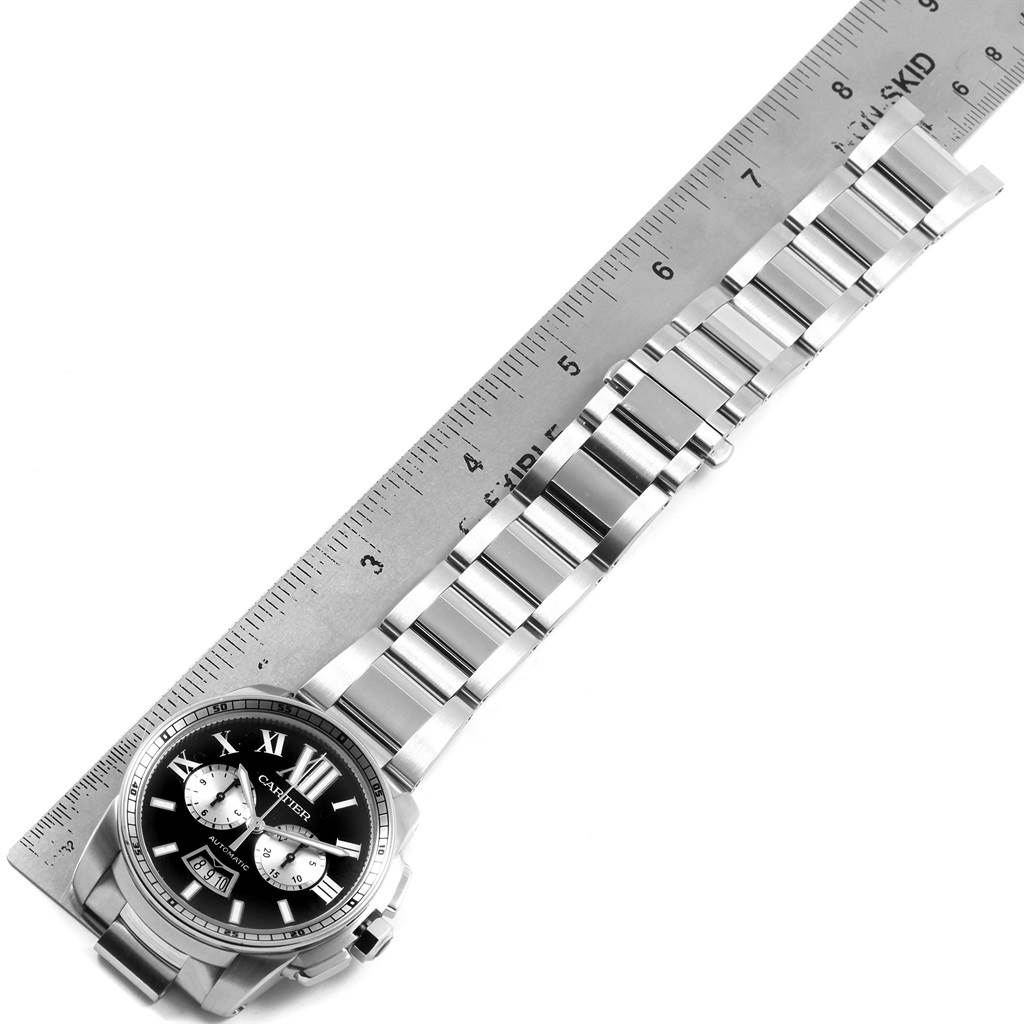 The image shows a Calibre de Cartier watch by Cartier, angled diagonally, featuring the watch face, bracelet, and partial clasp on a ruler.