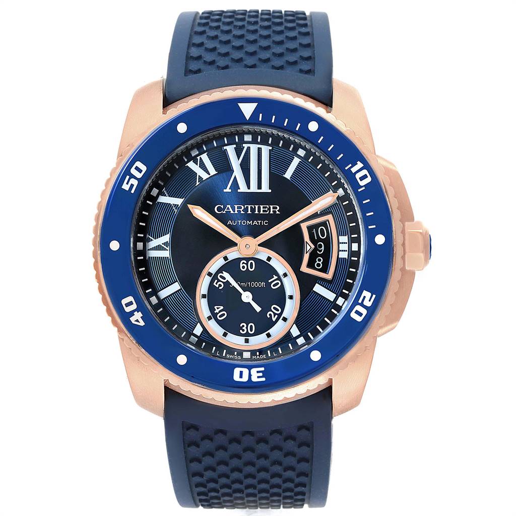 The image shows a front view of the Calibre de Cartier watch by Cartier, featuring a blue dial and bezel with gold accents and a rubber strap.