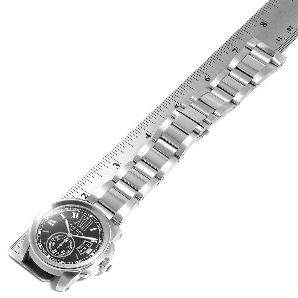 The image shows the Calibre de Cartier watch by Cartier at an angled top-down view with its bracelet aligned next to a ruler.