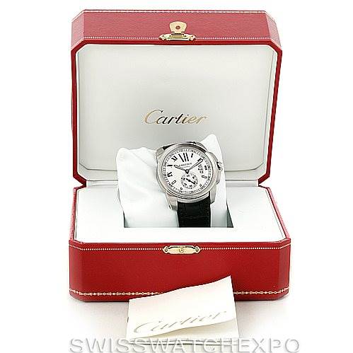The image shows a Calibre de Cartier watch by Cartier placed inside an open red box with a booklet visible in front.