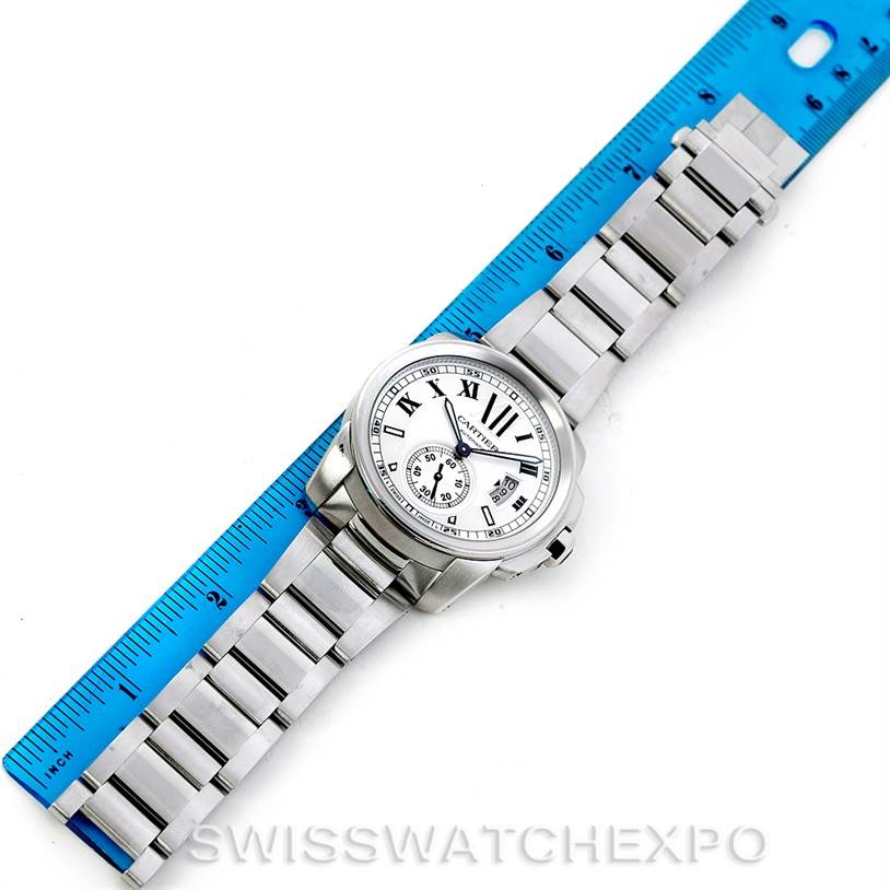 The Calibre de Cartier watch by Cartier is shown from a top-down angle, displaying its face, bezel, and entire bracelet next to a ruler.