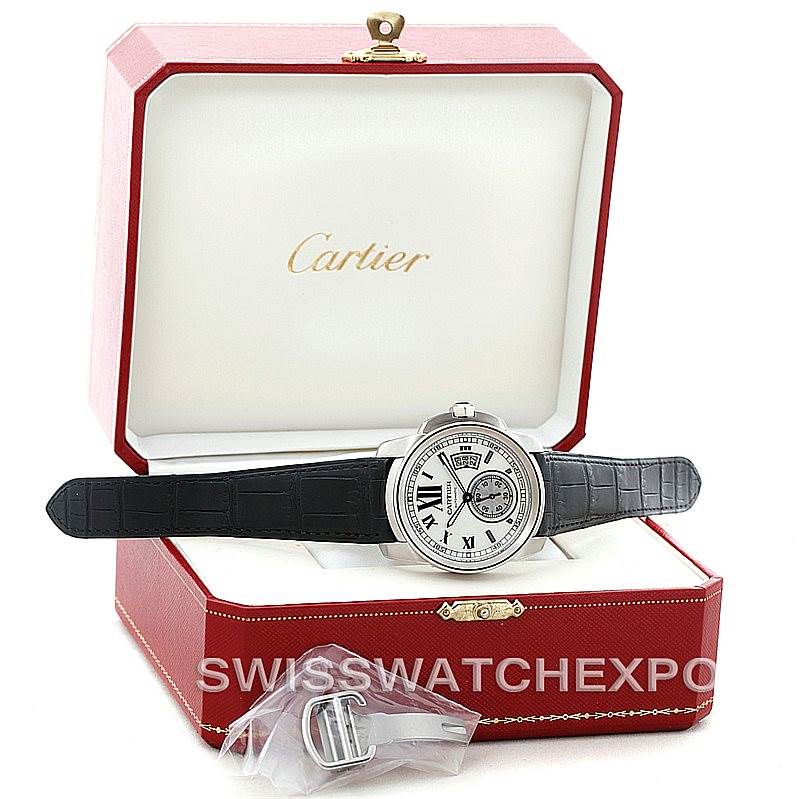 The Calibre de Cartier watch by Cartier is displayed in an open red box with a black strap and additional buckle accessory.
