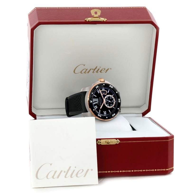 The image shows a Calibre de Cartier watch by Cartier at a front angle, inside its open display case, alongside a booklet.