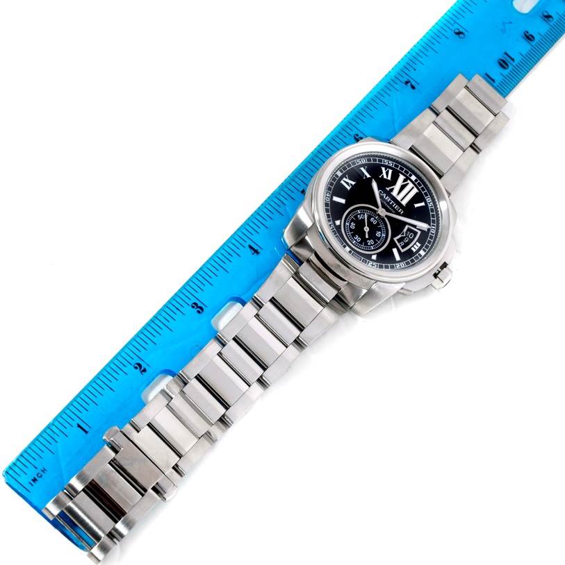 The Calibre de Cartier watch by Cartier is shown lying flat, displaying the dial, case, and metal bracelet against a ruler.