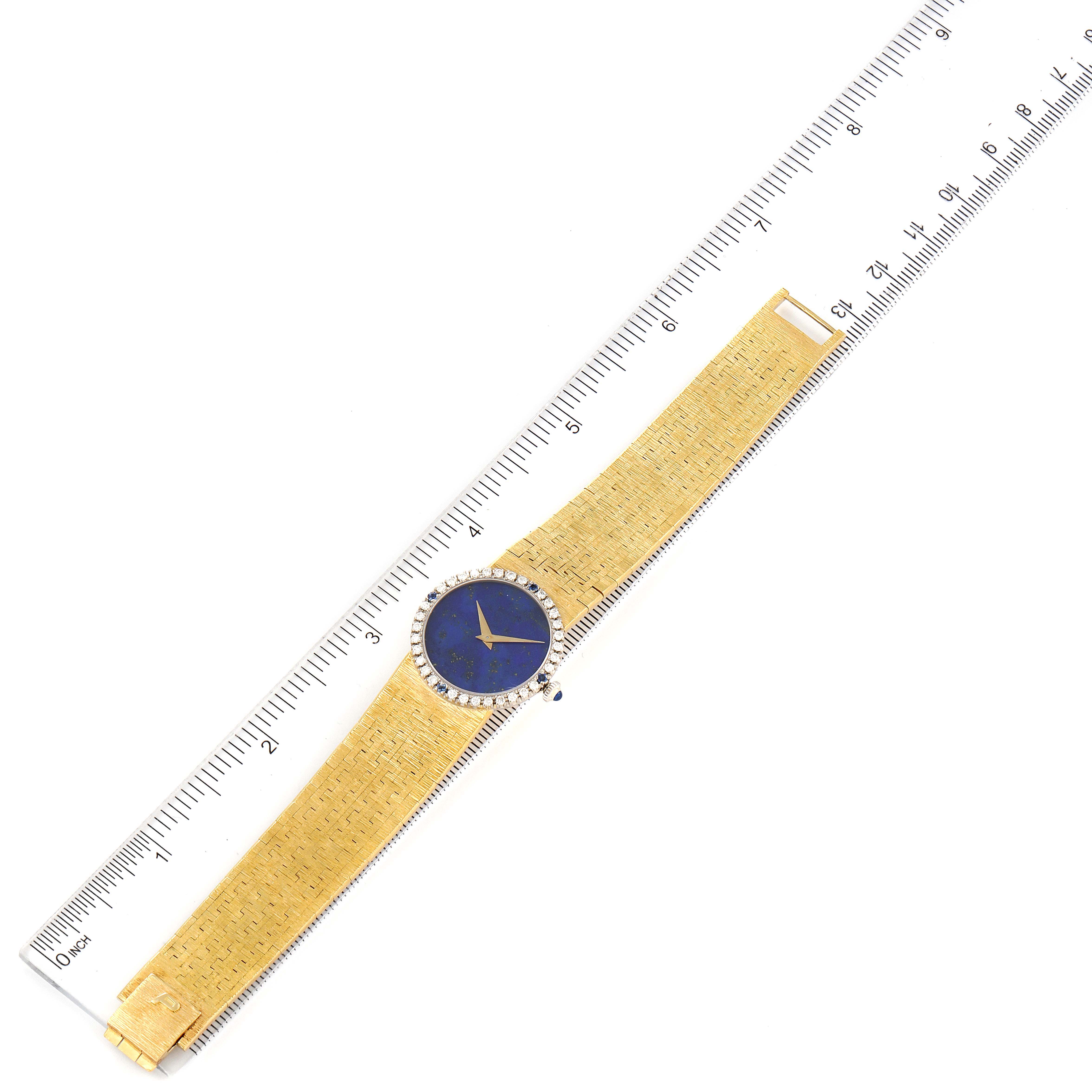 The image shows a top-down view of the Piaget 9706-A-6 Women's Yellow Gold Blue Dial 9706-A-6 Women's Yellow Gold Blue Dial model 9706 Yellow Gold Lapis Stone Dial Diamond Sapphire Vintage Cocktail Watch next to a ruler.