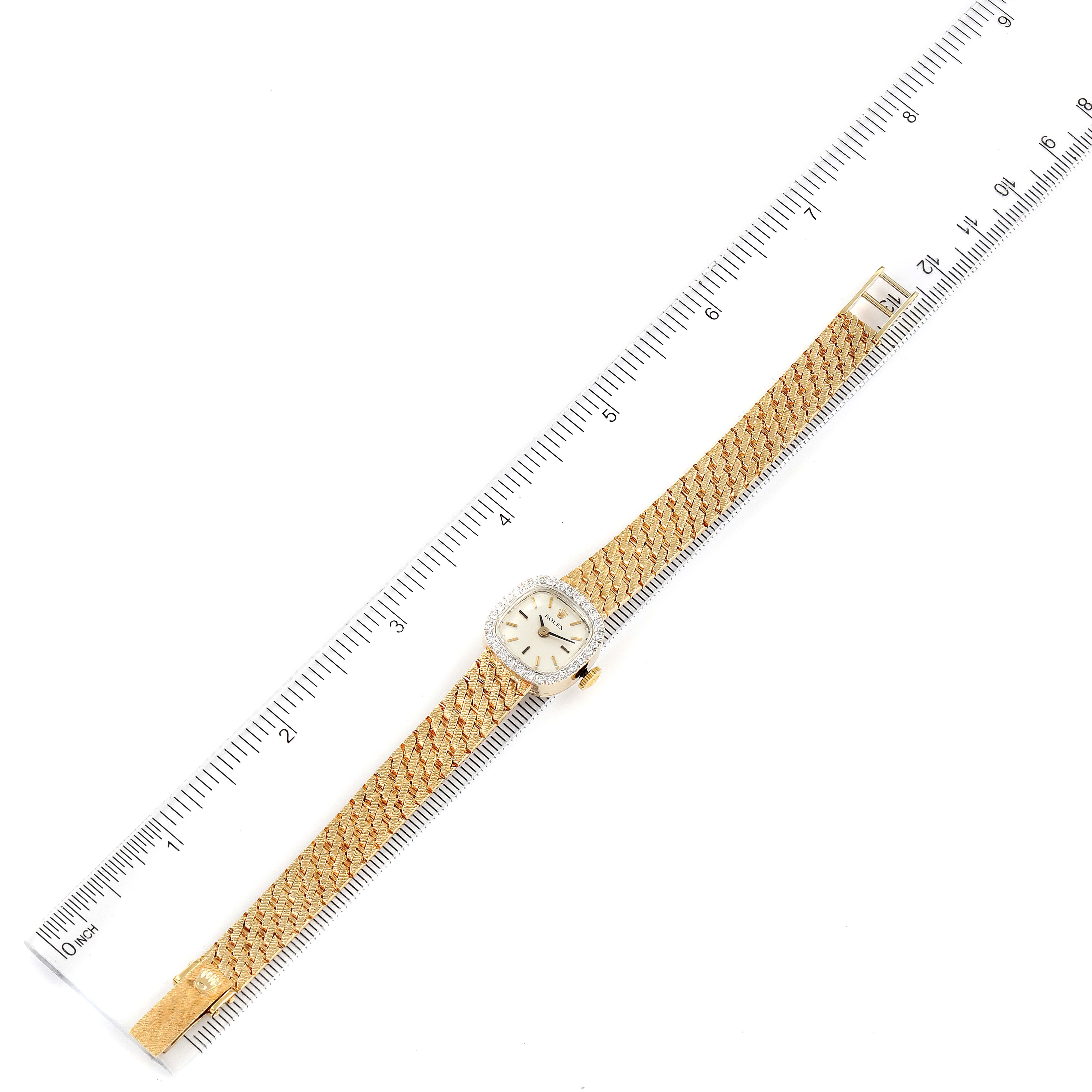 The image shows an aerial view of a Rolex Cocktail Women
s Yellow Gold Silver Dial Women
s Yellow Gold Silver Dial model watch, displaying the entire face, case, and band beside a ruler.