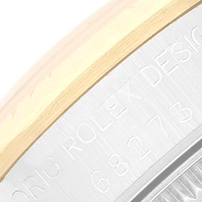 This image shows an angled close-up of the side of a Rolex Mid-Size 68273 Women
s Steel and Gold (two tone) Champagne Dial 68273 Women
s Steel and Gold (two tone) Champagne Dial watch with engraved text.