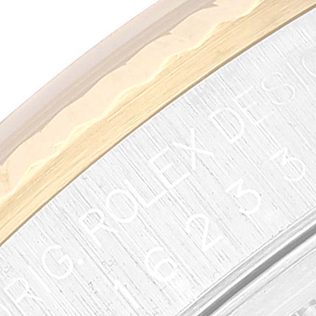 This close-up of a Rolex Datejust 16233 Men's Steel and Gold (two tone) Silver Dial 16233 Men's Steel and Gold (two tone) Silver Dial watch shows part of the bezel and some engraved text on the metal surface.