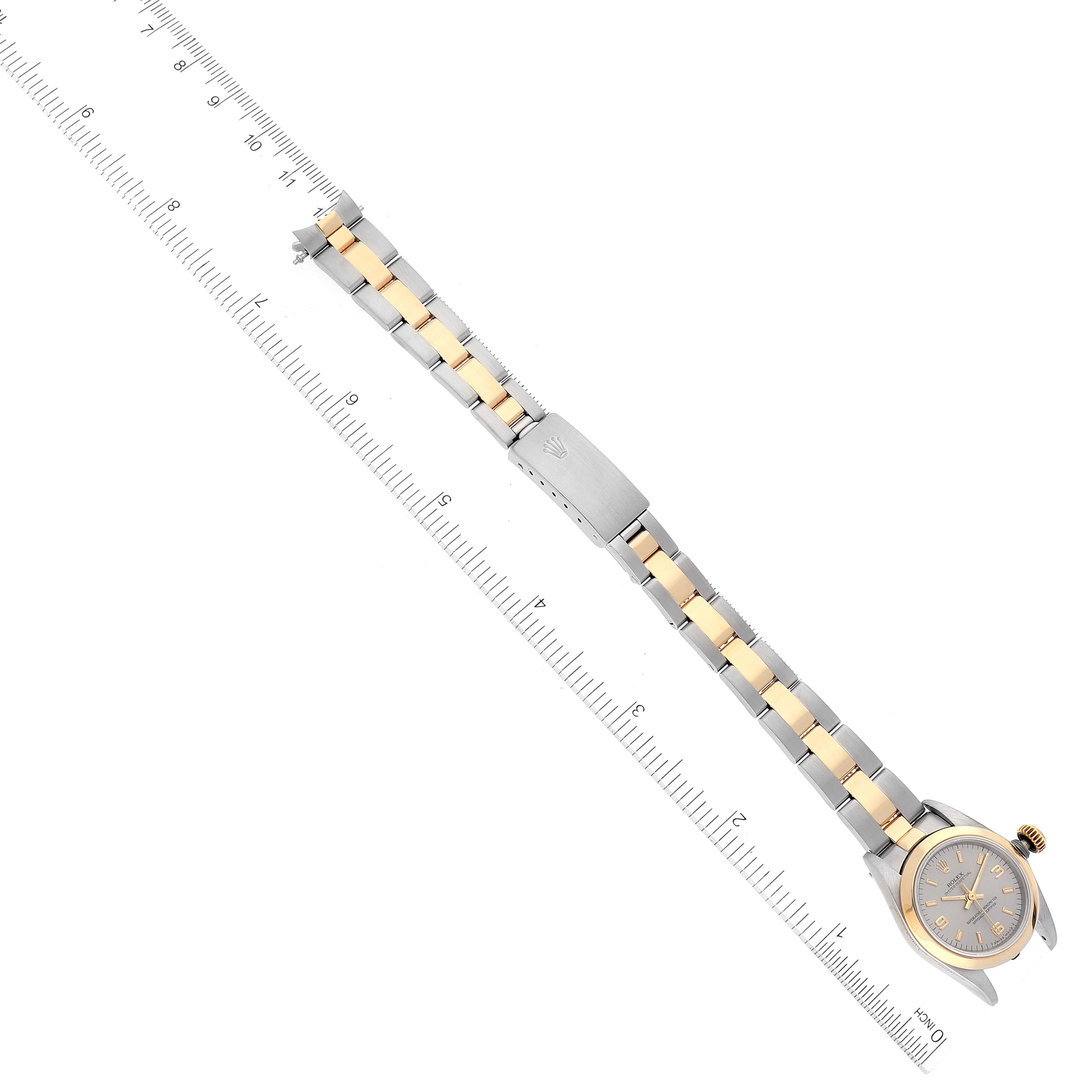 This image shows a Rolex Oyster Perpetual 67183 Women's Steel and Gold (two tone) Silver Dial 67183 Women's Steel and Gold (two tone) Silver Dial watch laid flat, highlighting its two-tone bracelet next to a ruler for scale.