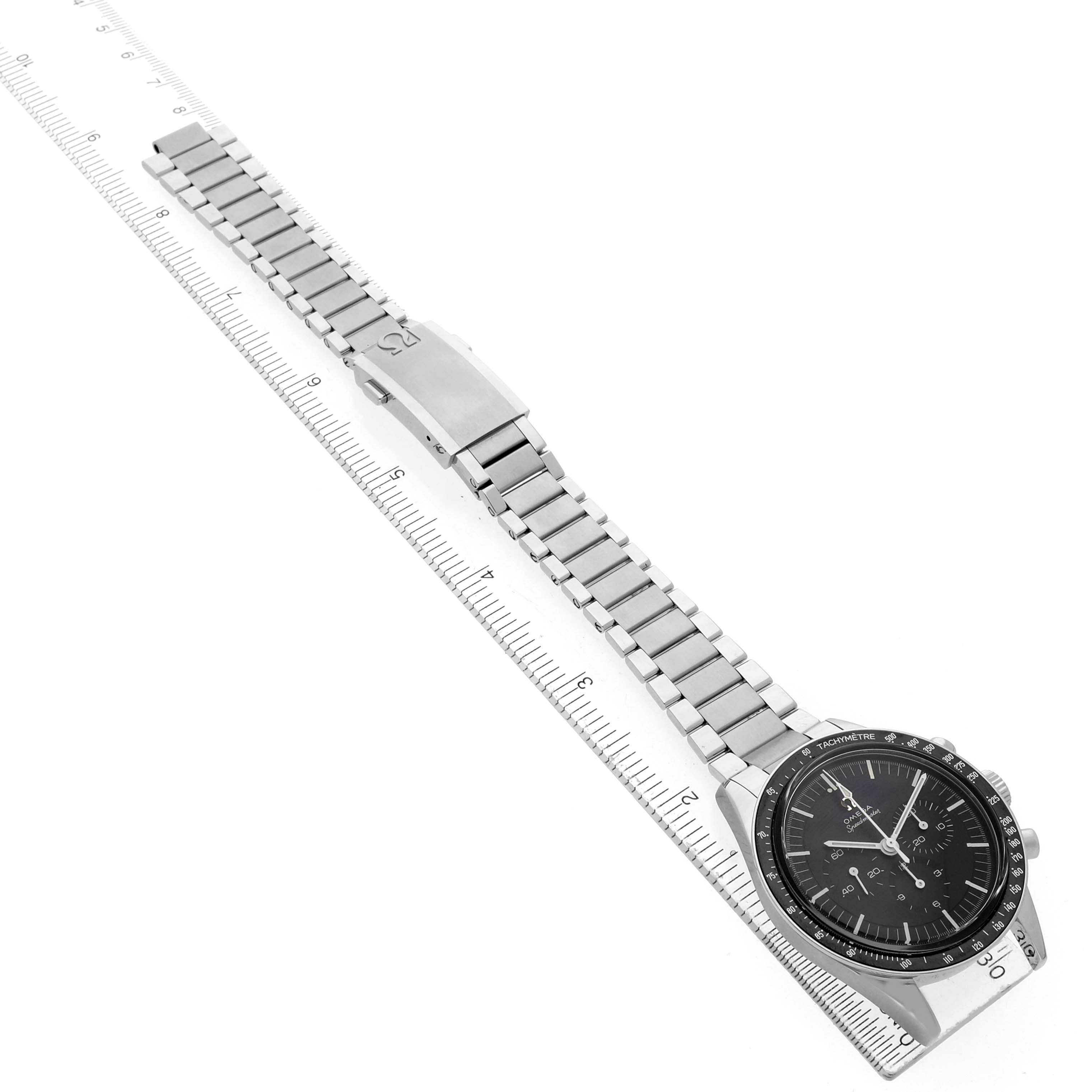 The Omega Speedmaster 311.30.40.30.01.001 Men's Stainless Steel Black Dial watch is shown at a close angle, displaying the face and full metal bracelet alongside a ruler for scale.