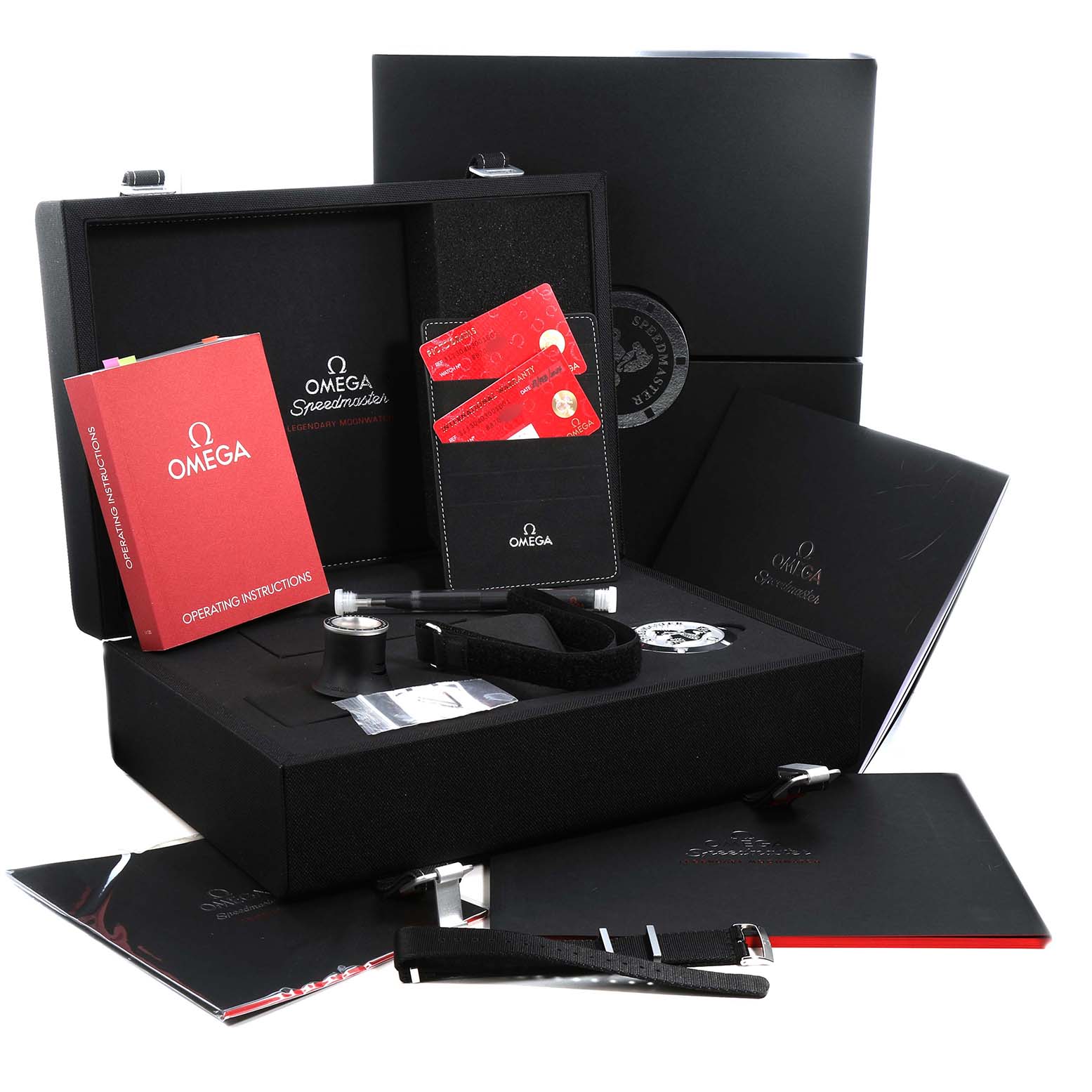 The image shows an Omega Speedmaster 311.30.40.30.01.001 Men's Stainless Steel Black Dial box set with manuals, a loupe, a strap, and cards, viewed from the front at a slight angle.