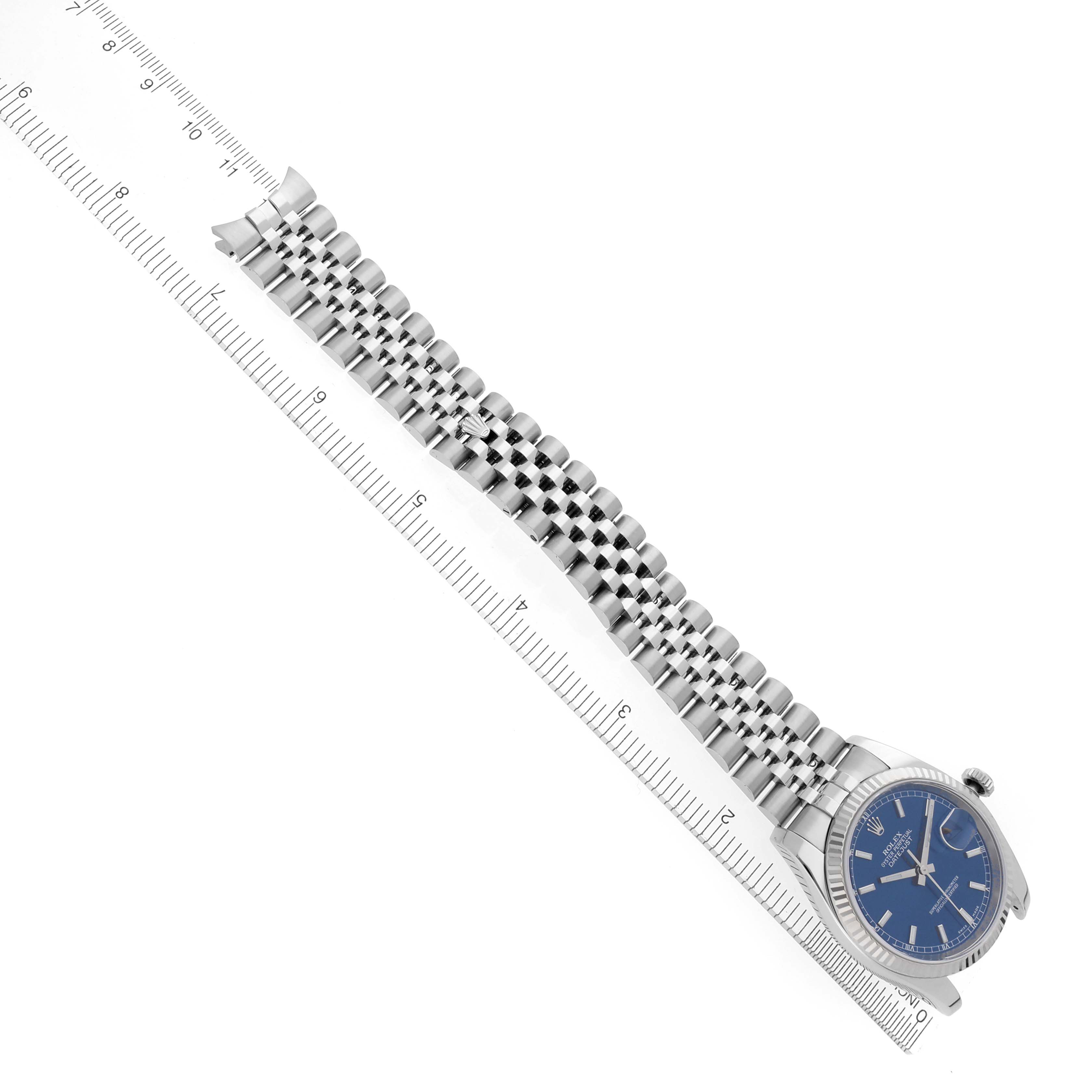 The Rolex Datejust 116234 Men's Stainless Steel Blue Dial 116234 Men's Stainless Steel Blue Dial watch is shown from an angled top view, displaying the face, bezel, and full bracelet alongside a ruler.