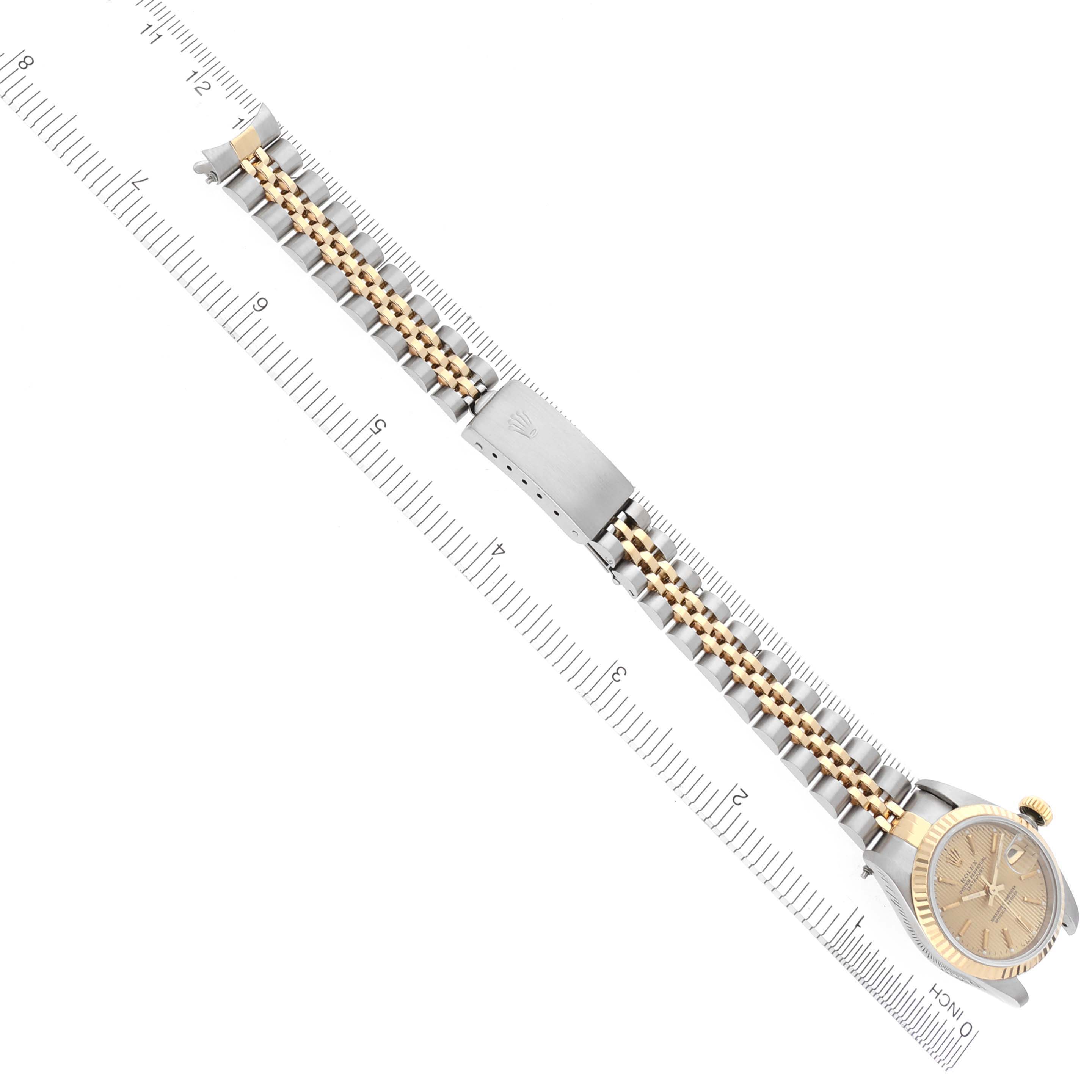 The Rolex Datejust 69173 Women's Steel and Gold (two tone) Champagne Dial 69173 Women's Steel and Gold (two tone) Champagne Dial watch is shown from a top view, highlighting the face, two-tone bracelet, and clasp on a ruler background.