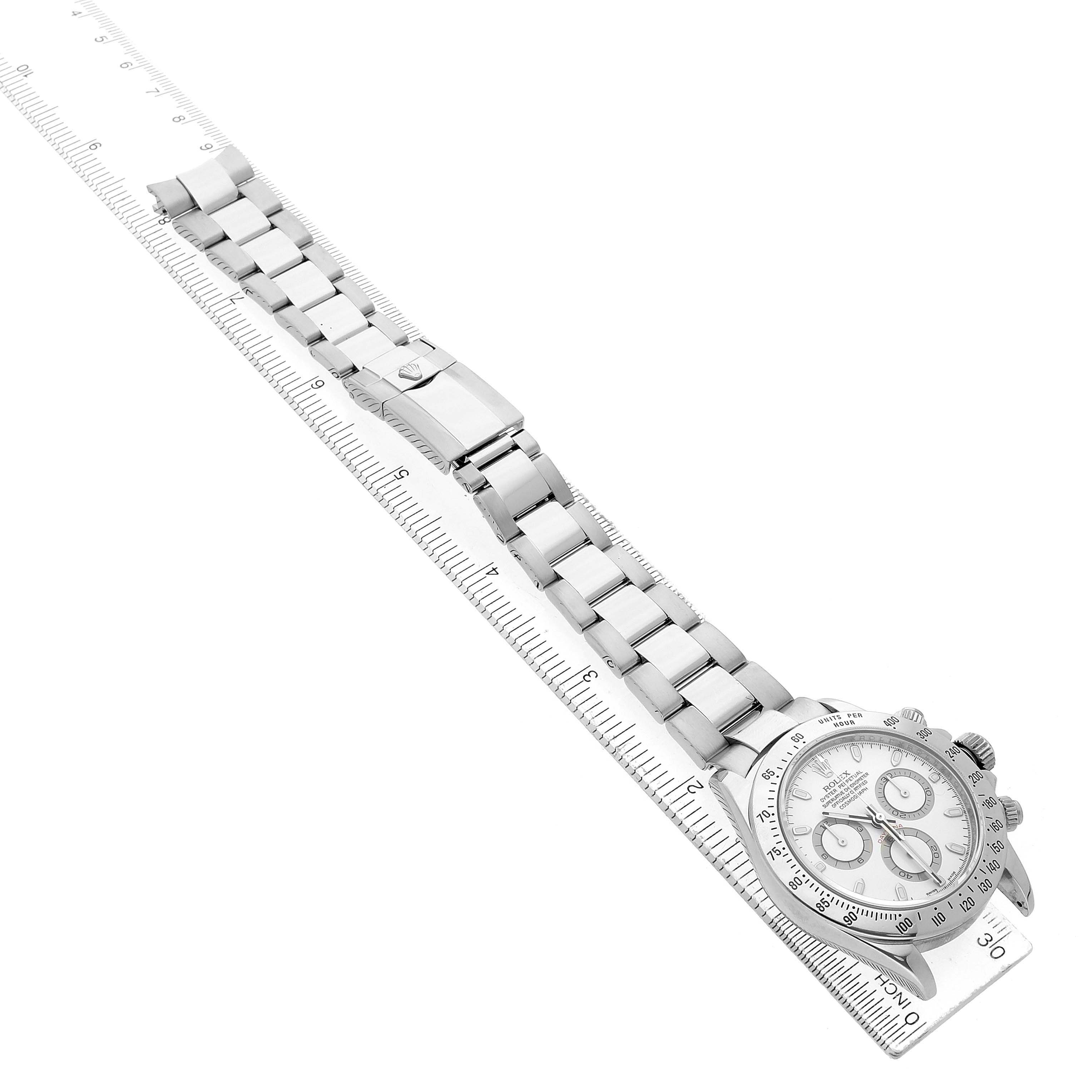 The Rolex Daytona 116520 Men's Stainless Steel White Dial watch is shown from a side angle, displaying the full bracelet and partial view of the dial on a ruler.