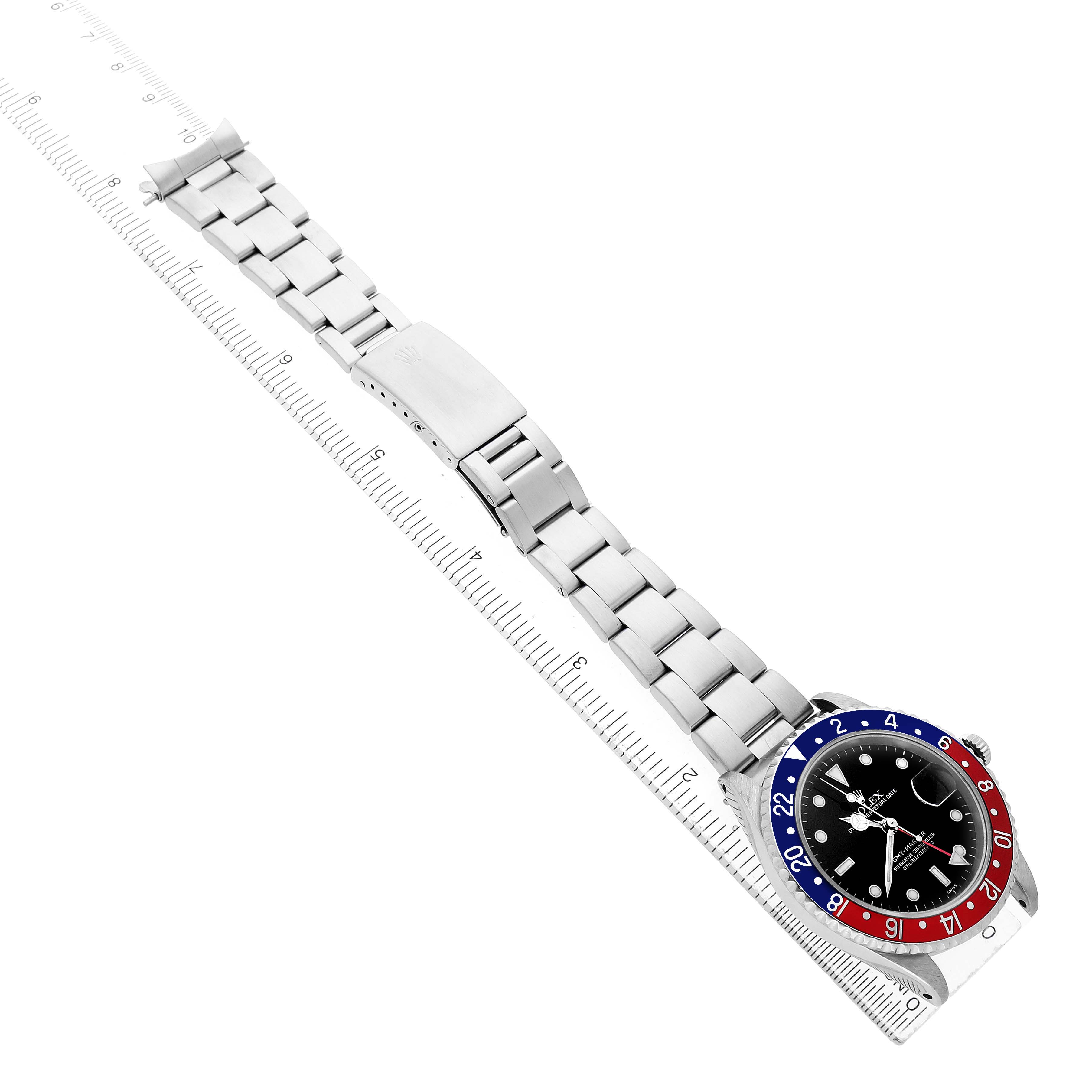 The Rolex GMT-Master 16700 Men's Stainless Steel Black Dial watch is shown at an angle with its bezel, dial, bracelet, and clasp visible, alongside a measuring ruler.