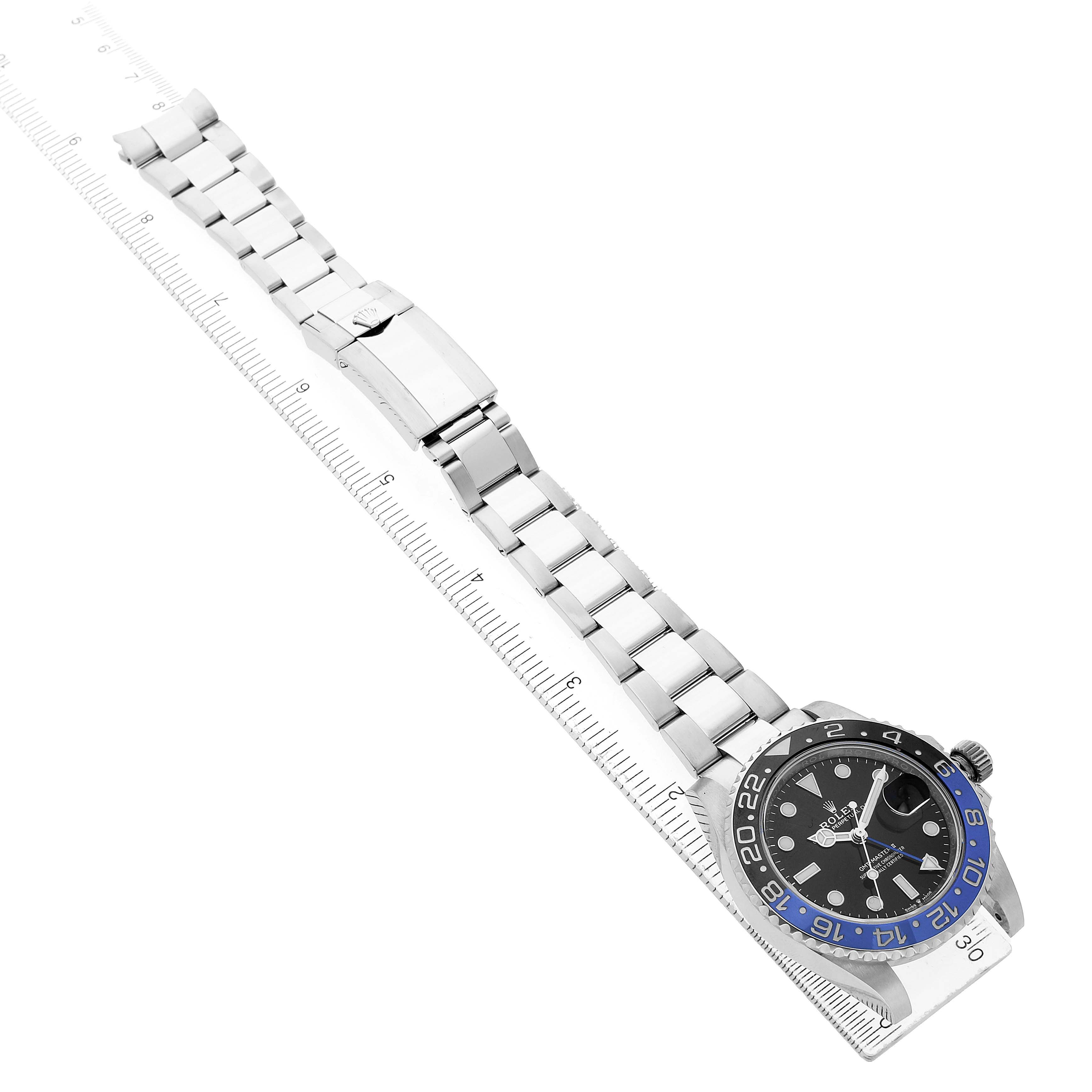 The Rolex GMT-Master 126710 Men's Stainless Steel Black Dial watch is shown from a top angle, displaying the dial, bezel, and full bracelet with clasp alongside a ruler.